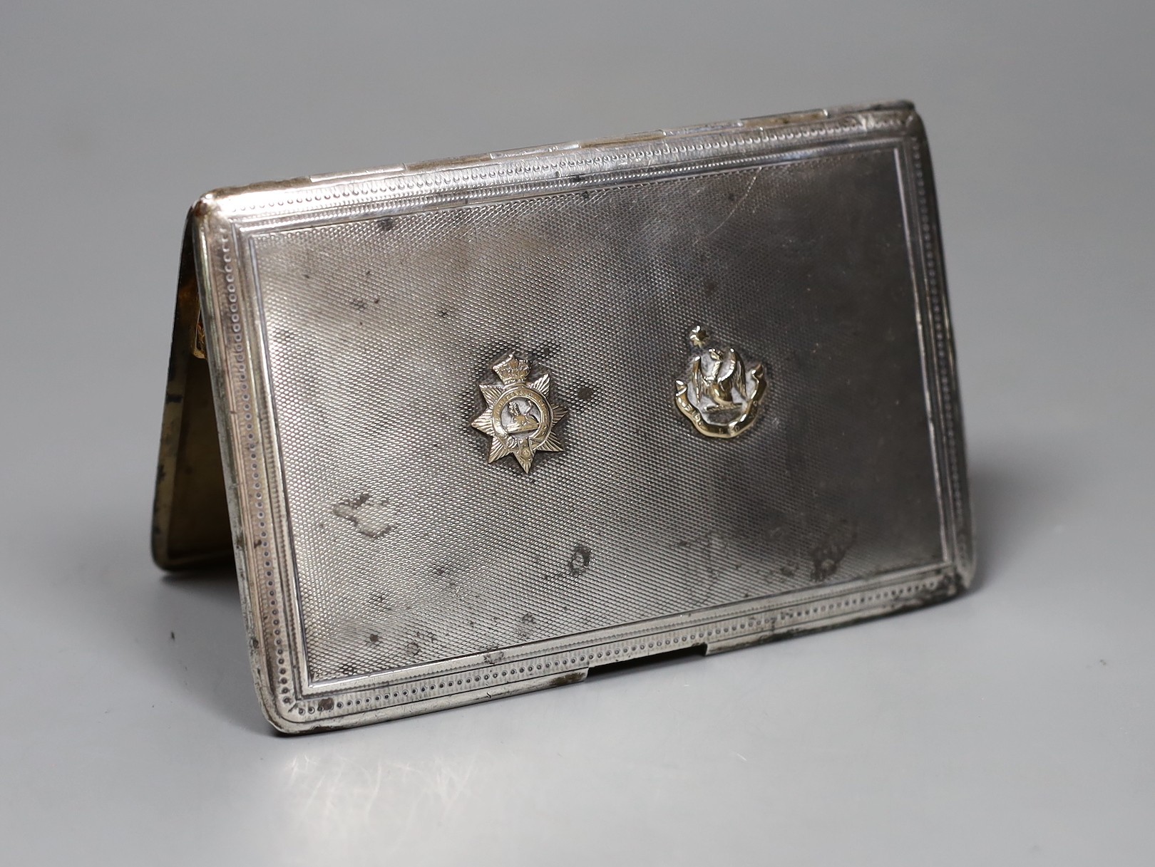 A Finnigans silver engine turned cigarette case with gilt interior mounted with gold Manchester Regiment 'Egypt' badge and family crest, London 1917, width 13cm